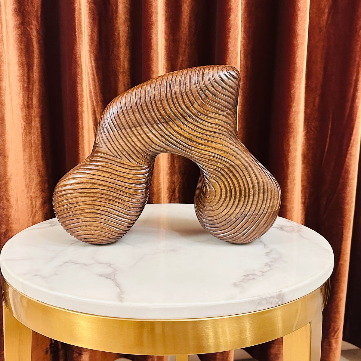 Decorative sculpture on a marble stool with gold base against a brown curtain background