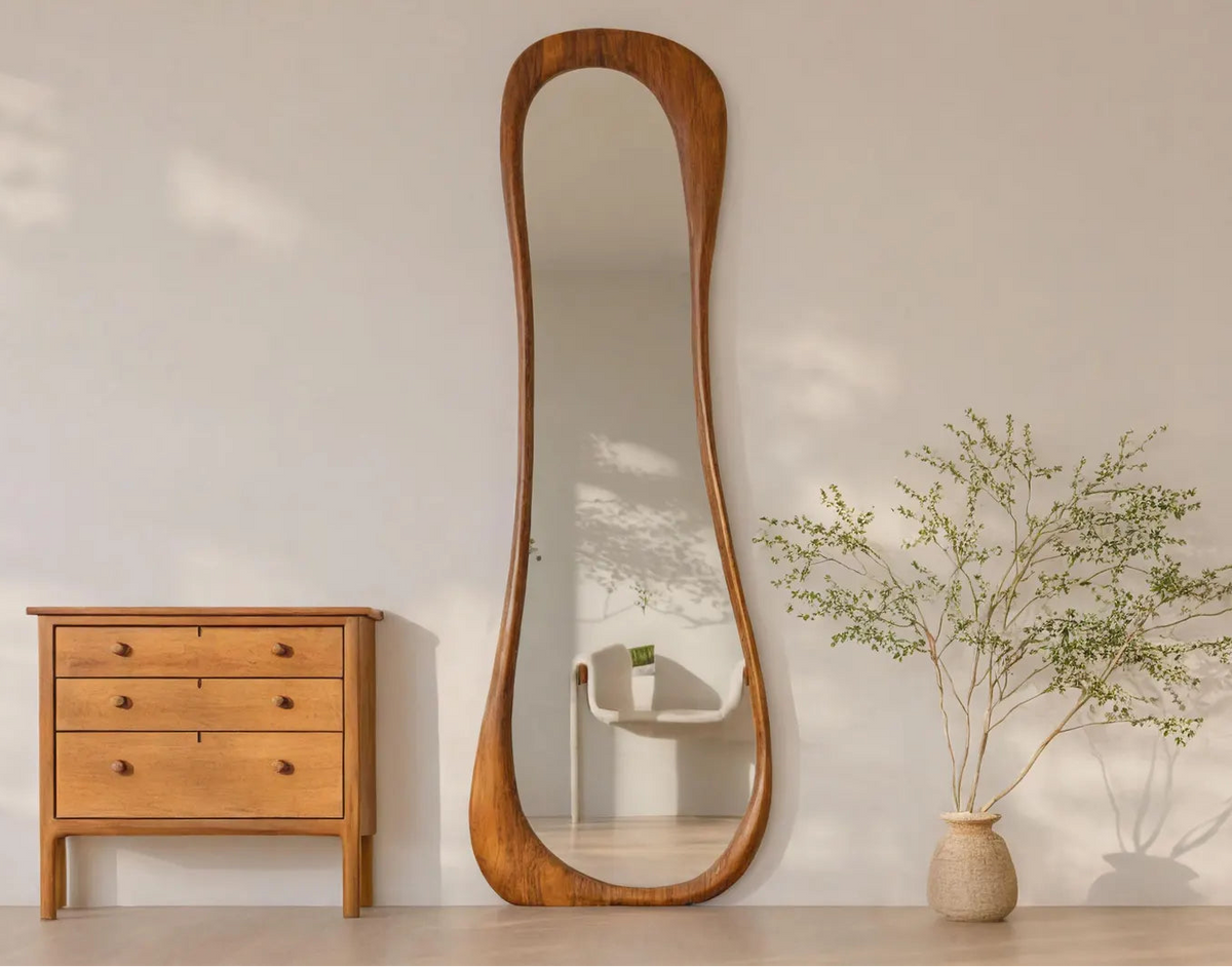 Wooden dresser and tall oval mirror in a room with a vase of plants.